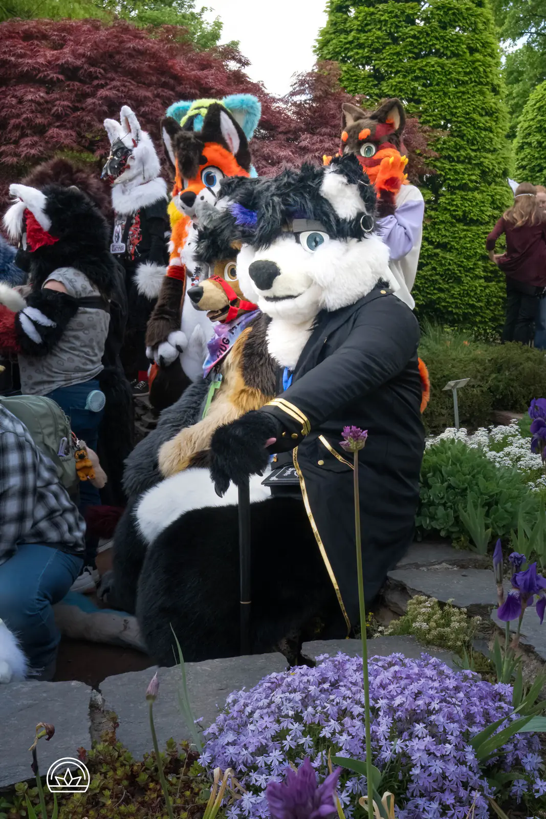 Eine Gruppe Furries mit und ohne Fursuit zwischen Bäumen und blühenden Blumen.