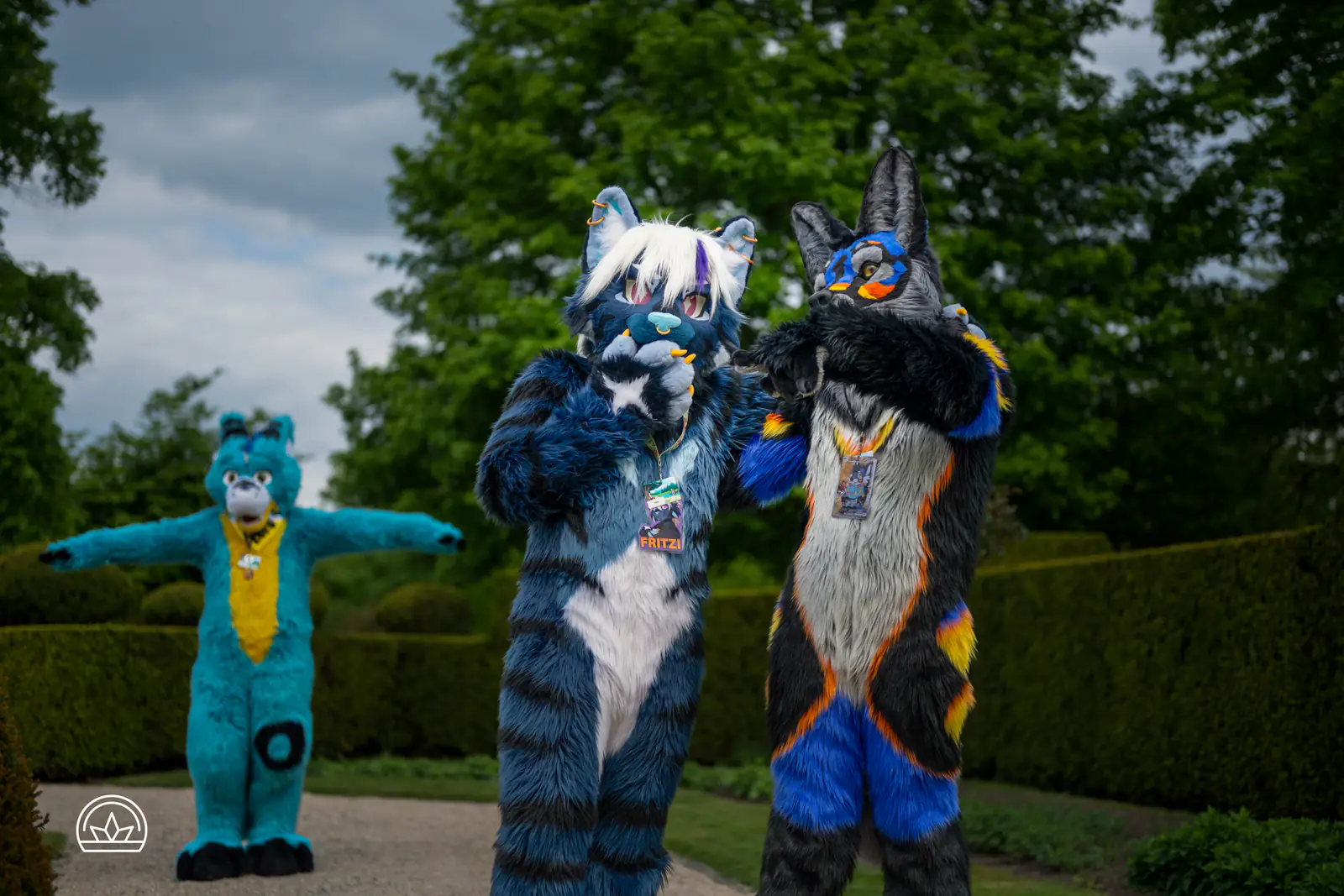 Zwei Fursuiter posieren im Grünen, hinter ihnen breitet ein weiterer fröhlich die Arme aus.